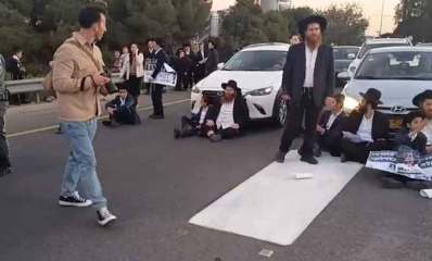 הפגנות וחסימות כבישים בבני ברק. חרדים יושבים על הכביש לפני מכוניות. שוטר עומד בצד.
