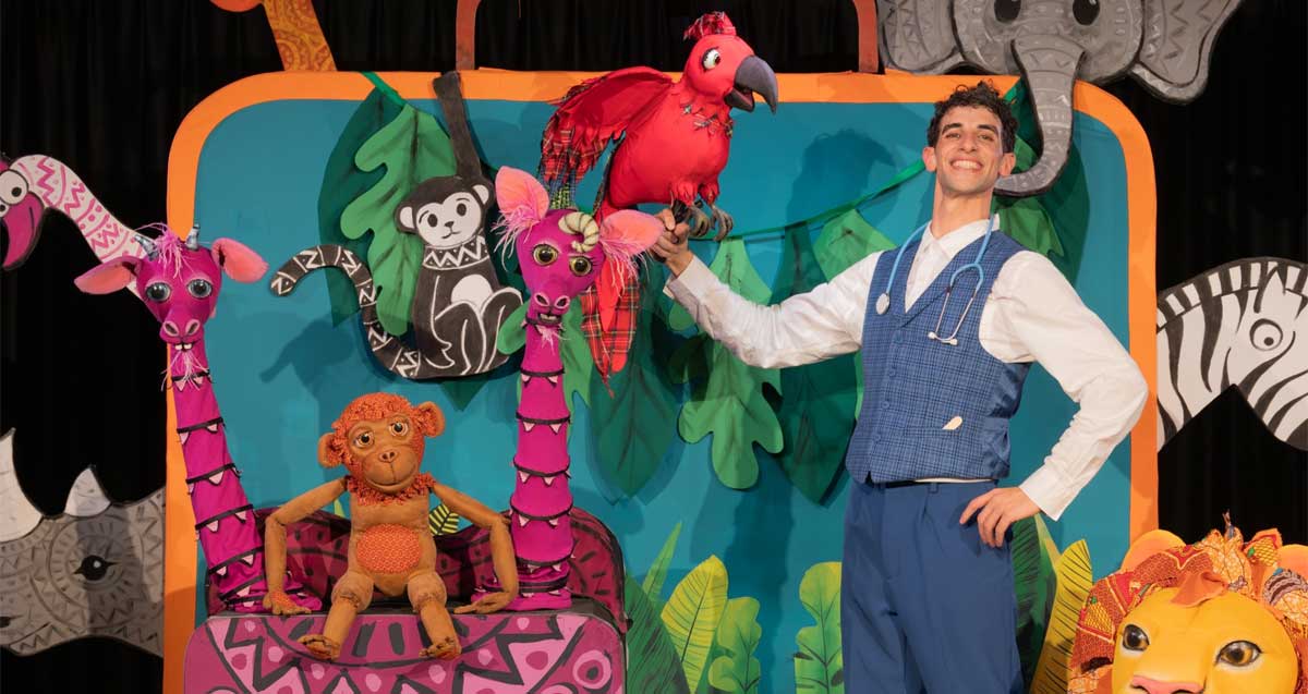 הצגת ילדים בסטודיו 24 גבעתיים. שחקן אוחז בובת תוכי, לידם בובות ג׳ירפה וחיות נוספות