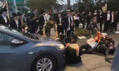 הפגנה בלתי חוקית בבני ברק. מפגינים יושבים ושוכבים על הכביש לפני מכוניות. מפגינים רבים עומדים על פס ההפרדה בין שני המסלולים של הכביש.