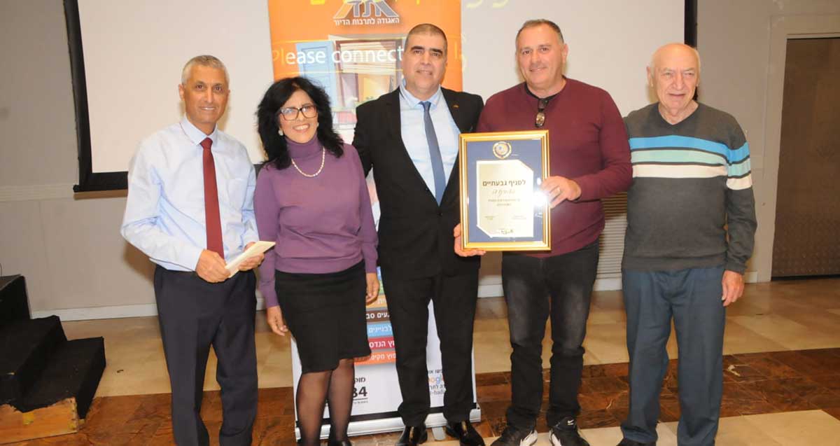 סניף גבעתיים של האגודה לתרבות הדיור נבחר למצטיין המחוזי. אישה וארבעה גברים בתמונה קבוצתית. אחד אוחז תעודה ממוסגרת.