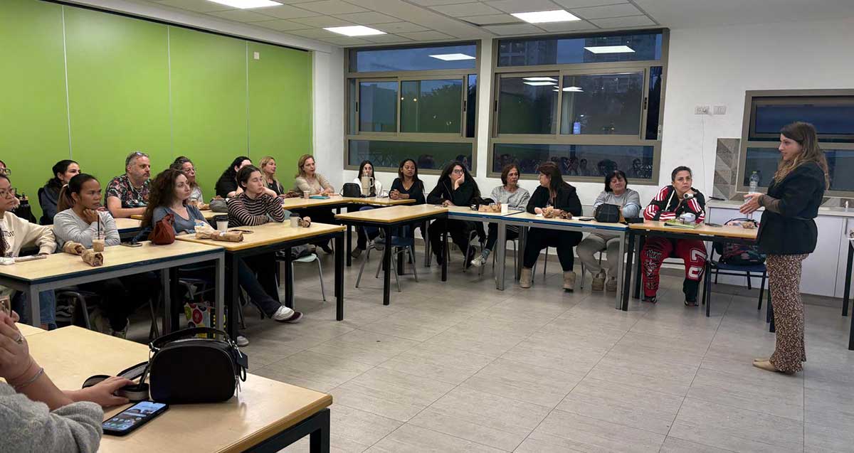 קורס מחנכות-מטפלות רביעי בגבעתיים. בכיתת לימוד יושבות ליד שולחנות המסודרים בצורת האות ח'. מולם עומדת מדריכה.