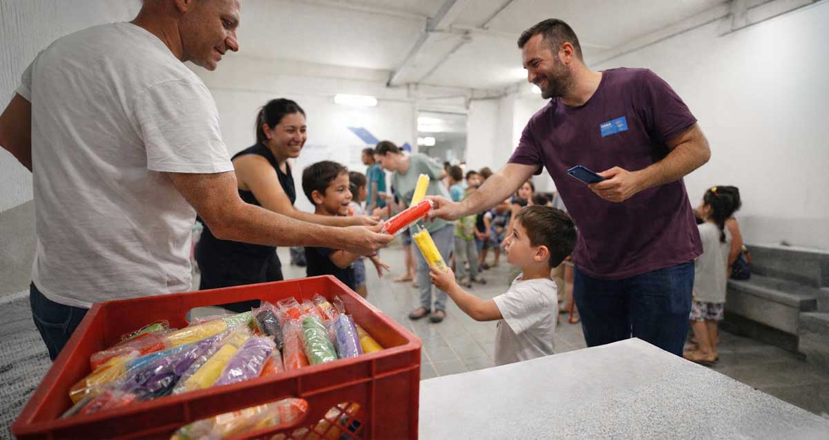 "מבצע ארטיק" במקלטים ברמת גן. איור AI. איש מחלק ארטיקים לילדים ולמבוגרים, מתוך ארגז פלסטיק מלא בארטיקים,