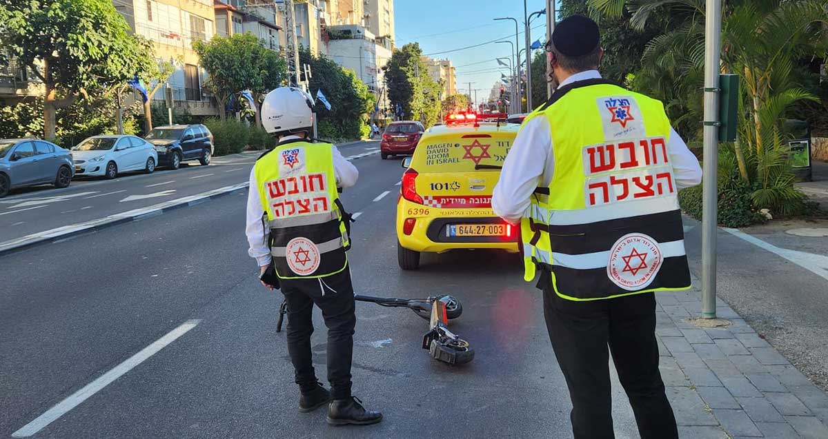 נער רוכב קורקינט נפגע בתאונת דרכים ברמת גן. שני חובשים של ארגון הצלה ליד קורקינט המונח על הכביש. מכונית של מגן דוד לפני הקורקינט.