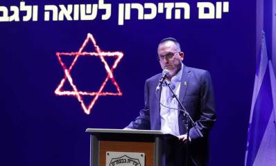 רן קוניק בטקס יום הזיכרון לשואה ולגבורה. עומד ליד דוכן נואמים שעליו שלט: עיריית גבעתיים, ומאחוריו מוקרן מגן דוד וכיתוב: יום הזיכרון לשואה ולגבורה