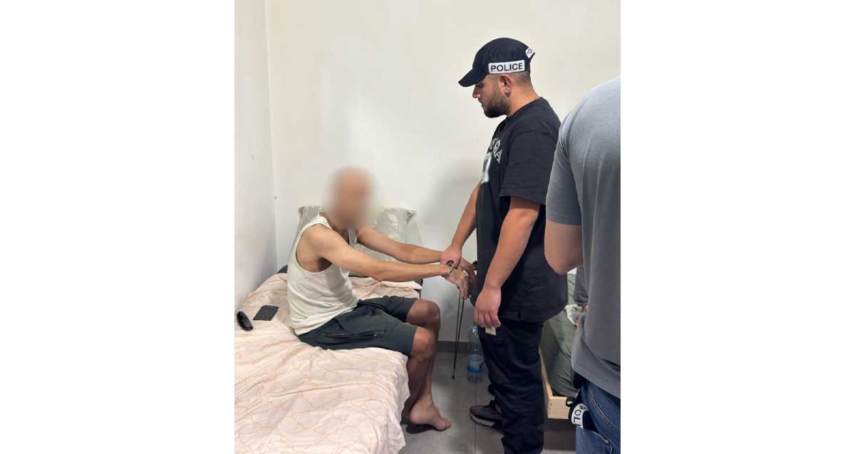 תושב רמת גן חשוד בניפוץ דלתות מערכת חדשות 12. שוטר אוזק את החשוד היושב על מיטה.