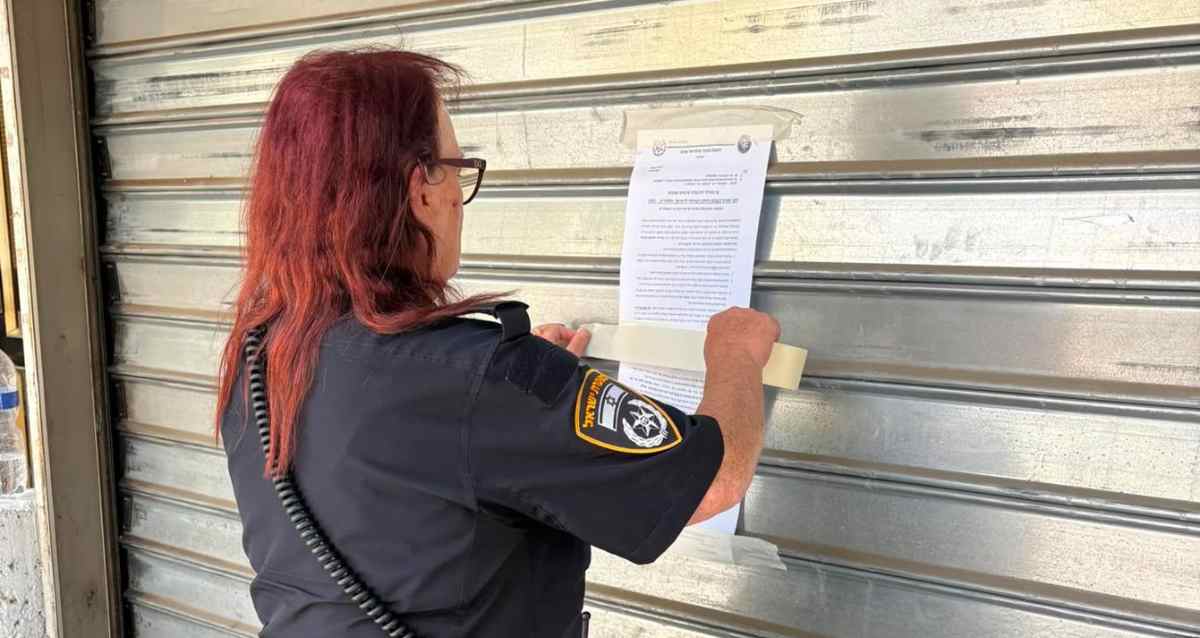 שוטרת מדביקה צו סגירה על חזית המרכול, צילם: משטרה