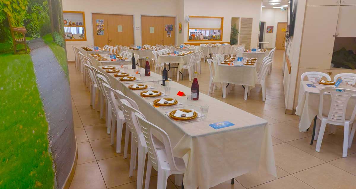סעודת ראש השנה העירונית. באולם שולחנות ערוכים עם מפות לבנות, צלחות כוסות ובקבוקי יין.
