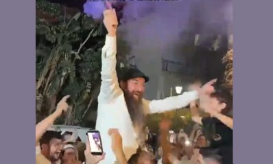 הרב יוסף דלויה בחגיגות מונף על כתפיים של אדם אחר עם עשן סגול בידו